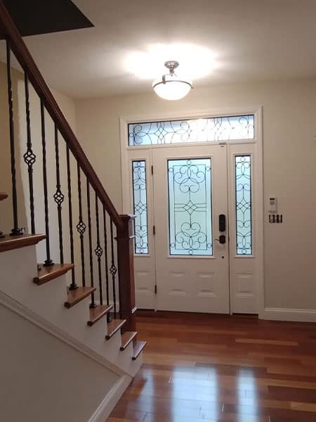 Elegant home entryway featuring a decorative glass door, hardwood floors, and a staircase with wrought iron railings. A fresh house painting job enhances the bright, welcoming atmosphere.