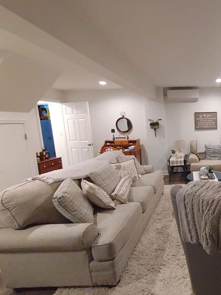 Cozy living room with a large beige sofa, patterned throw pillows, and a light-colored rug. A desk with a mirror sits against the wall, complementing the home's interior design. Perfect inspiration for house painting projects.